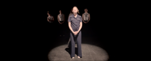 Person stands in spotlight in dark space.